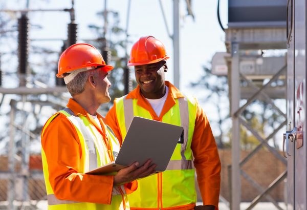 happy electricians using laptop computer in electrical substation